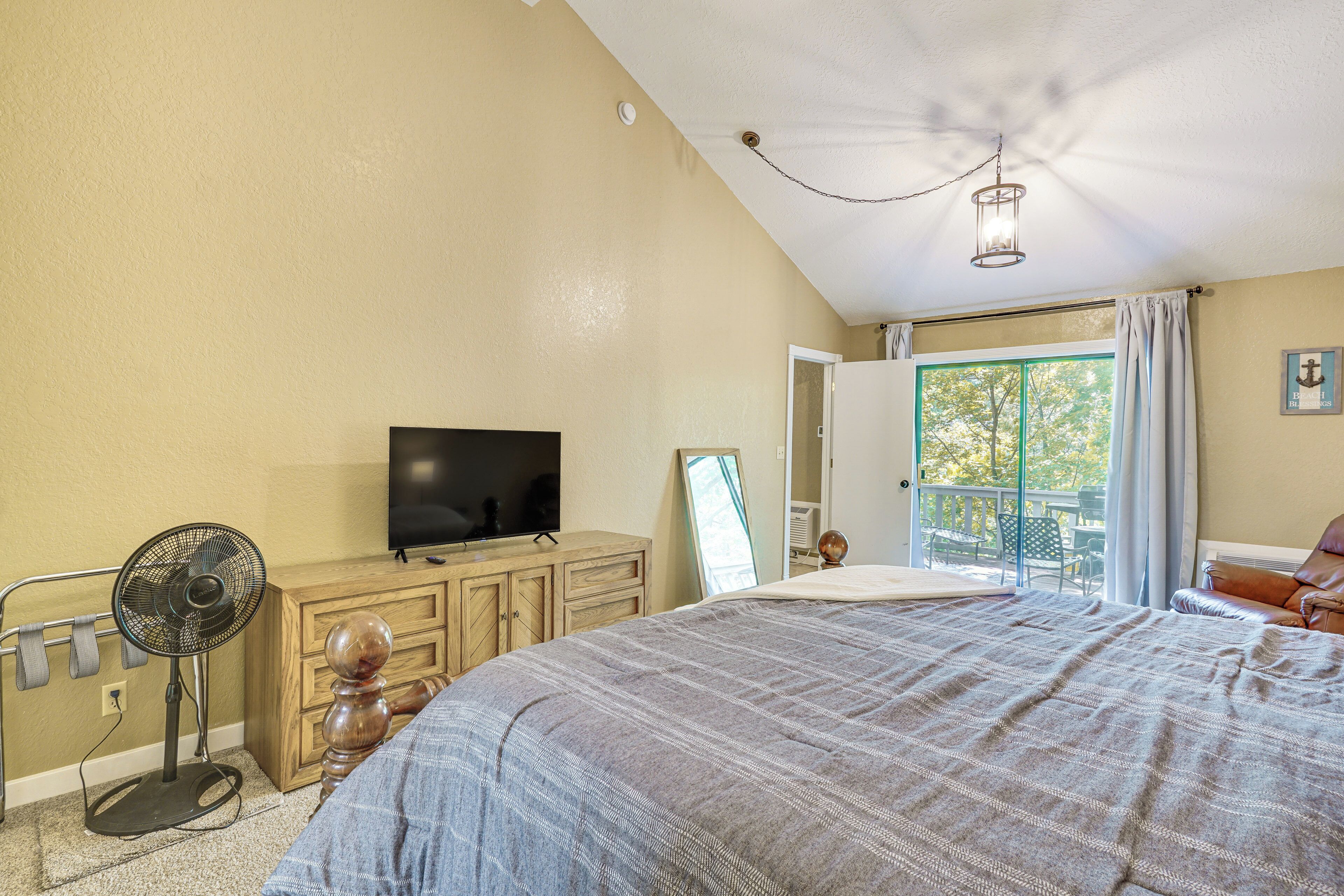 A bedroom with a bed, a television, a fan, a dresser, and a door leading to a balcony.