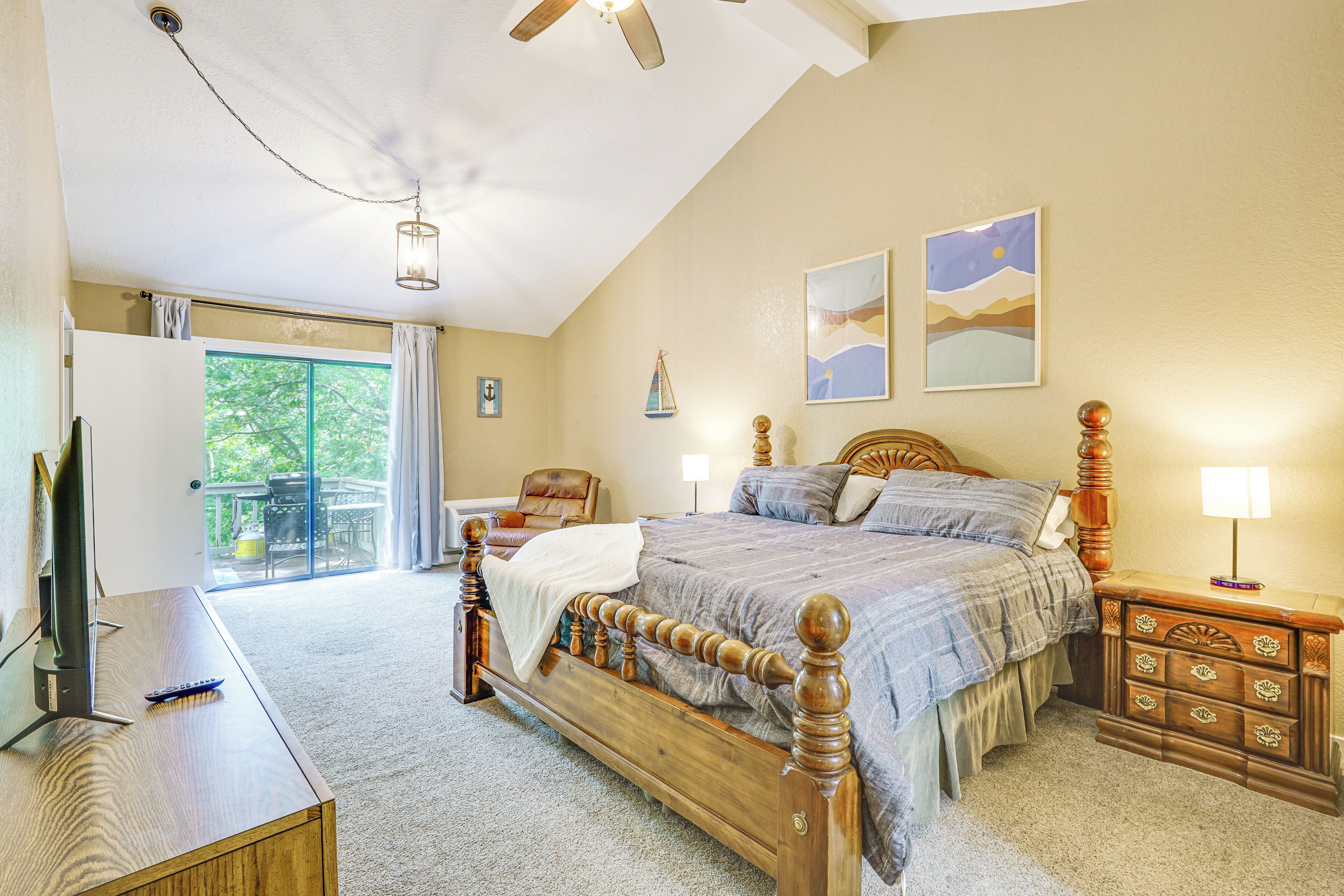 A bedroom with a bed, wooden headboard, bedside tables, a TV, and a balcony with a view.