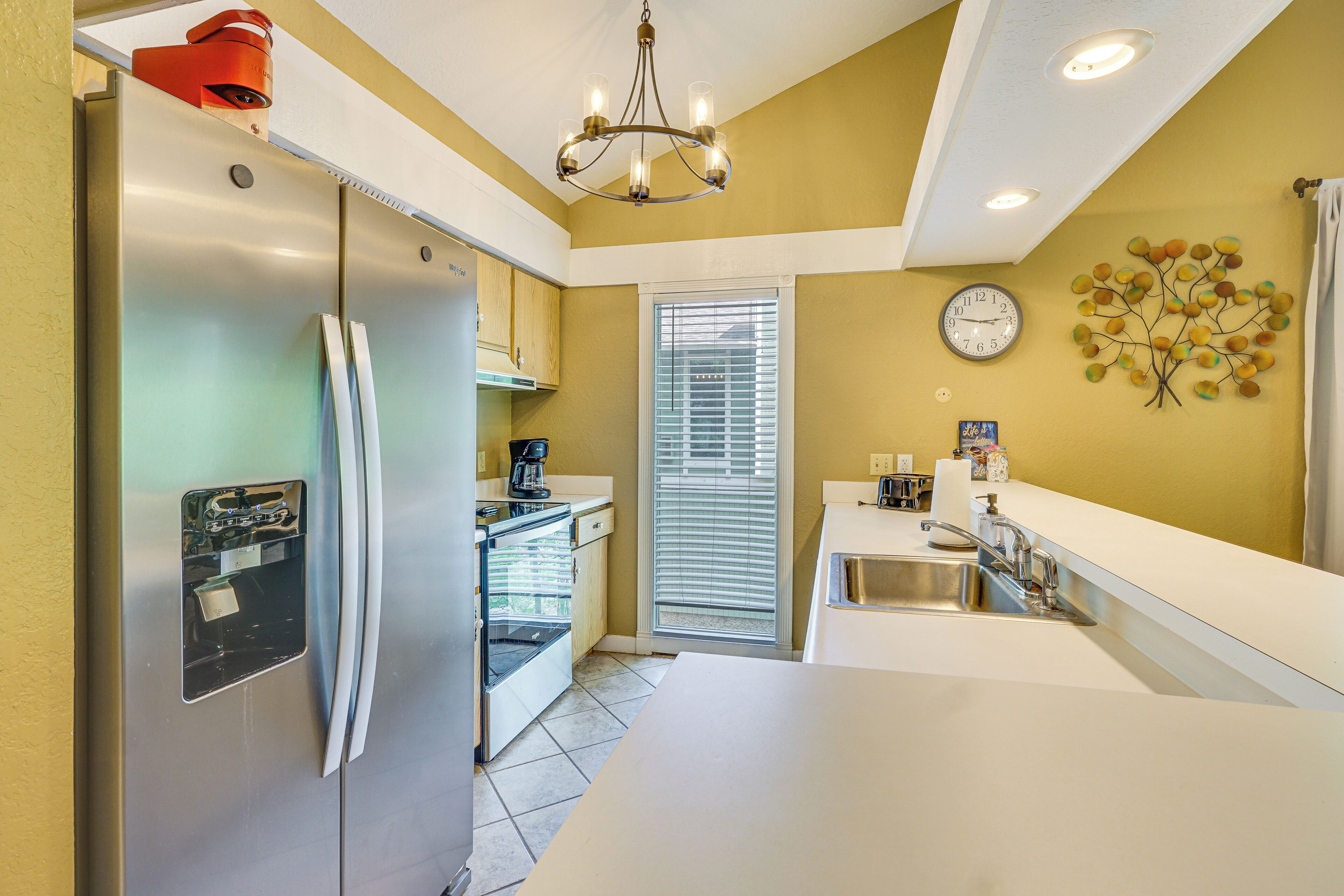 A compact kitchen with a refrigerator, oven, sink, and a clock on the wall.