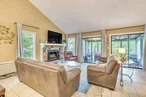 A living room with a fireplace, two sofas, a coffee table, and a view through large windows.