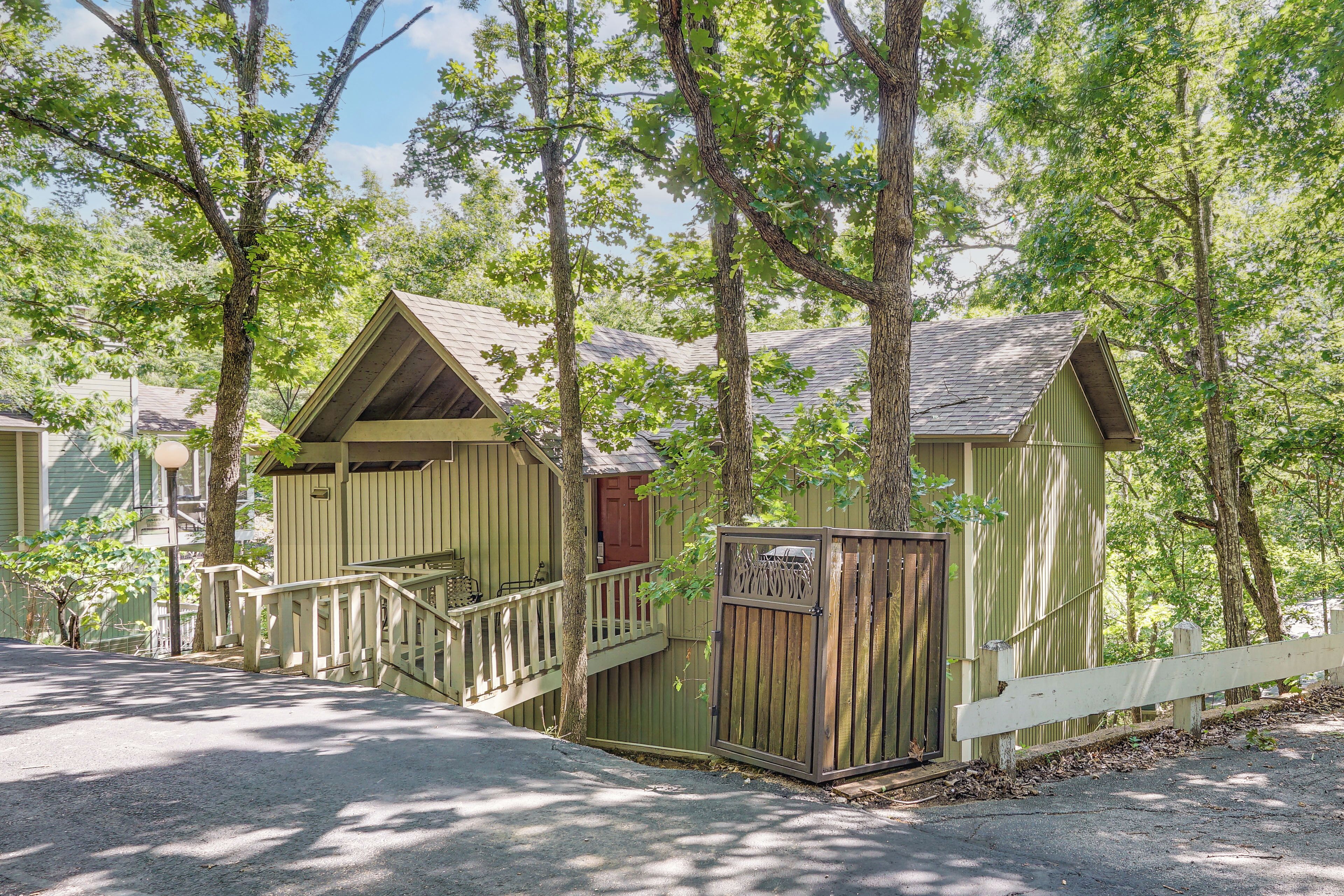 A row of wooden cabins with a porch and a small staircase, surrounded by trees.