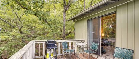 A wooden deck with outdoor furniture, a grill, and a glass door leading to an interior space.