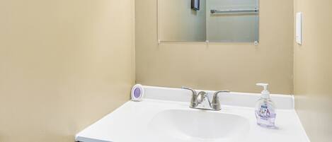 A bathroom with a white sink, a mirror, and a hand soap dispenser.