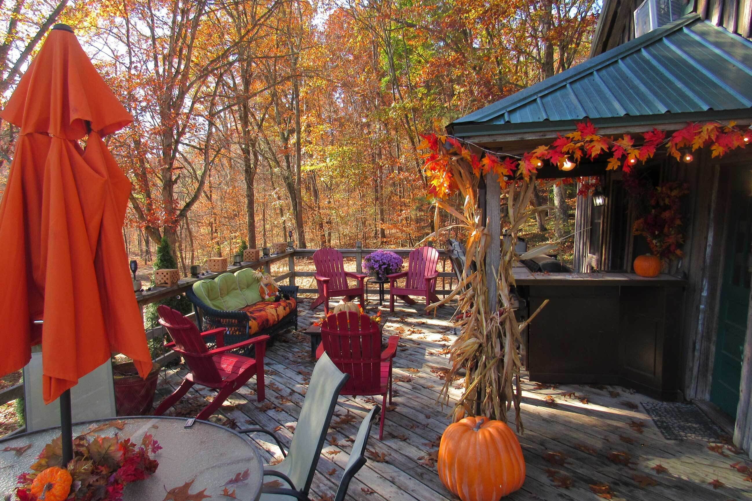An outdoor patio with red chairs, a table, and a covered area with autumn decorations.