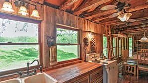 Une cuisine rustique aux murs en bois, dotée d’une grande fenêtre et d’un poêle d’époque.