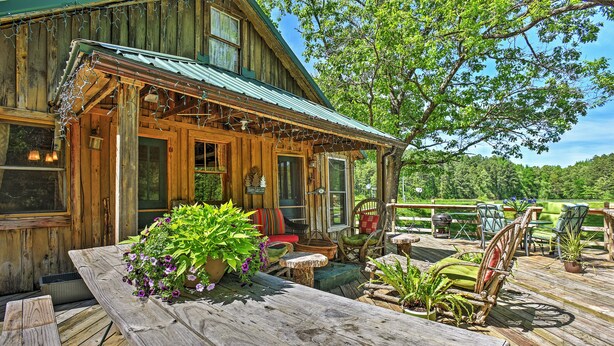 Un chalet rustique en bois, doté d’une véranda, de meubles de jardin et offrant une vue sur un paysage verdoyant et luxuriant.