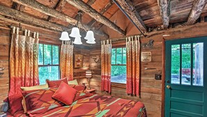 Une chambre dans un chalet en rondins, avec un lit, des rideaux, une lampe et une porte verte.