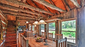 L’intérieur d’un chalet rustique en bois comprend un coin repas, un escalier en bois et de grandes fenêtres qui offrent une vue sur l’extérieur.