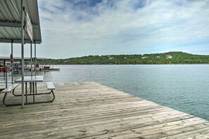 A wooden dock extending into calm water with a covered picnic table and a metal railing.
