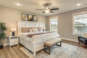 A bedroom with a bed, bedside tables, a ceiling fan, a window, and a view of the outside.