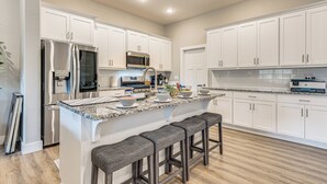 A modern kitchen with white cabinetry, stainless steel appliances, a granite countertop, and a central island with bar stools. - Family-friendly Ozark Villa - Centrally Located (Ozark)