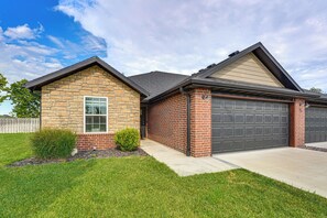 A two-story house with a stone facade and a brick extension, featuring a garage and a small front yard.
