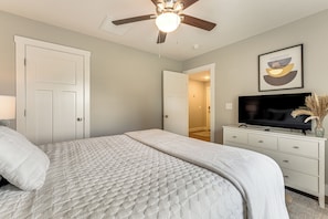 Une chambre à coucher avec un lit, un ventilateur de plafond, un téléviseur et un tableau encadré au mur.