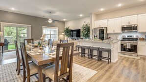 Une cuisine moderne avec des meubles blancs, des appareils en acier inoxydable et un coin repas comprenant des chaises et une table en bois.