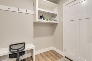 Quarto nos fundos com uma escrivaninha branca, uma cadeira, uma prateleira com produtos de limpeza e uma porta branca.