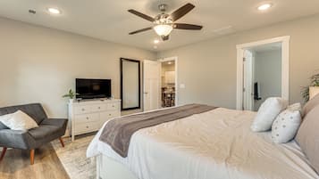 A bedroom with a bed, a TV, a chair, a dresser, and a ceiling fan.