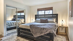 A bedroom with a bed, a bedside table, a mirror, and a window with blinds. - Pet & Family Friendly Cottage Near the Lake! (Osage Beach)