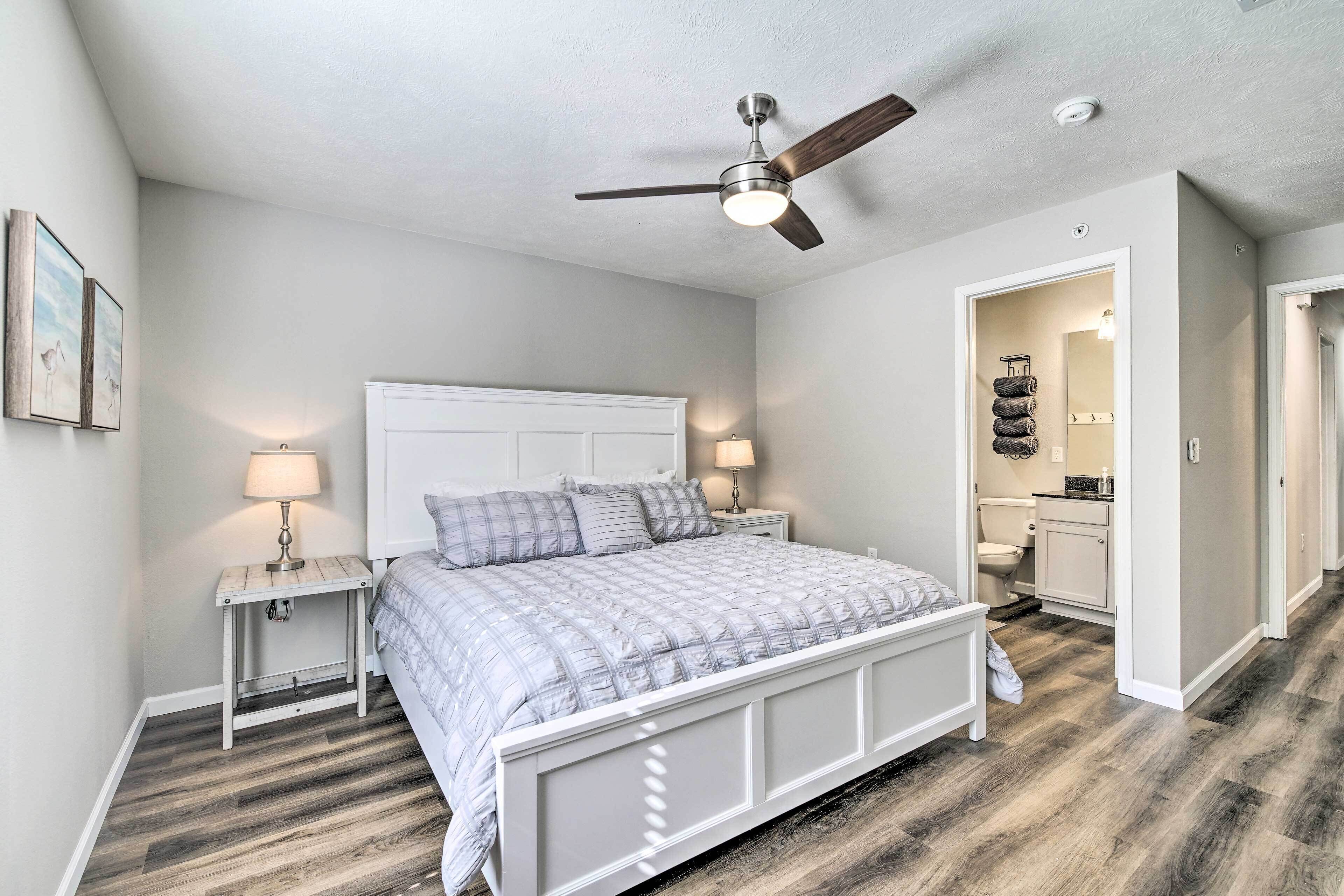 A bedroom with a bed, nightstands, a ceiling fan, and a bathroom visible through an open door.