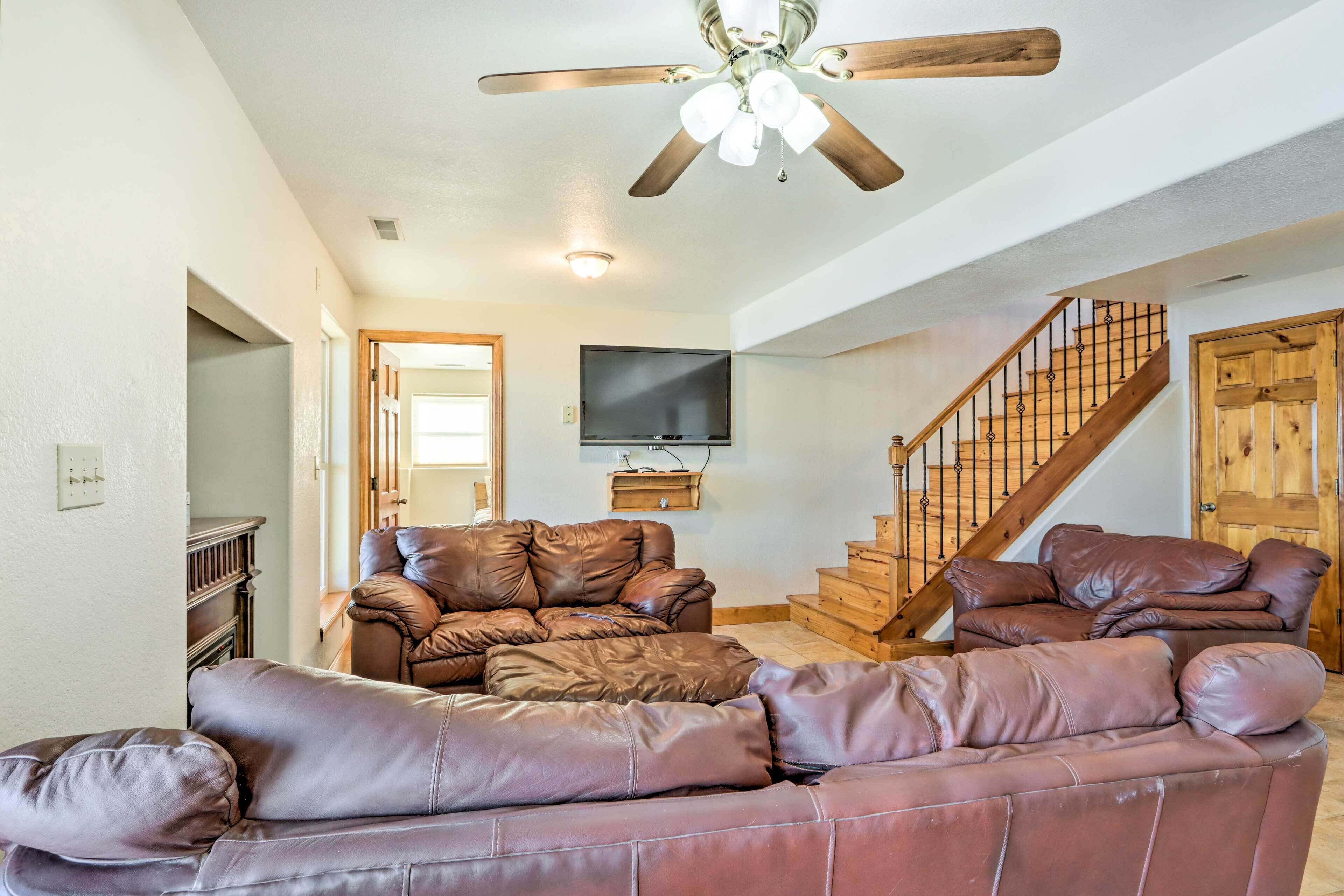 A living room with leather sofas, a ceiling fan, a flat-screen TV, and a staircase.