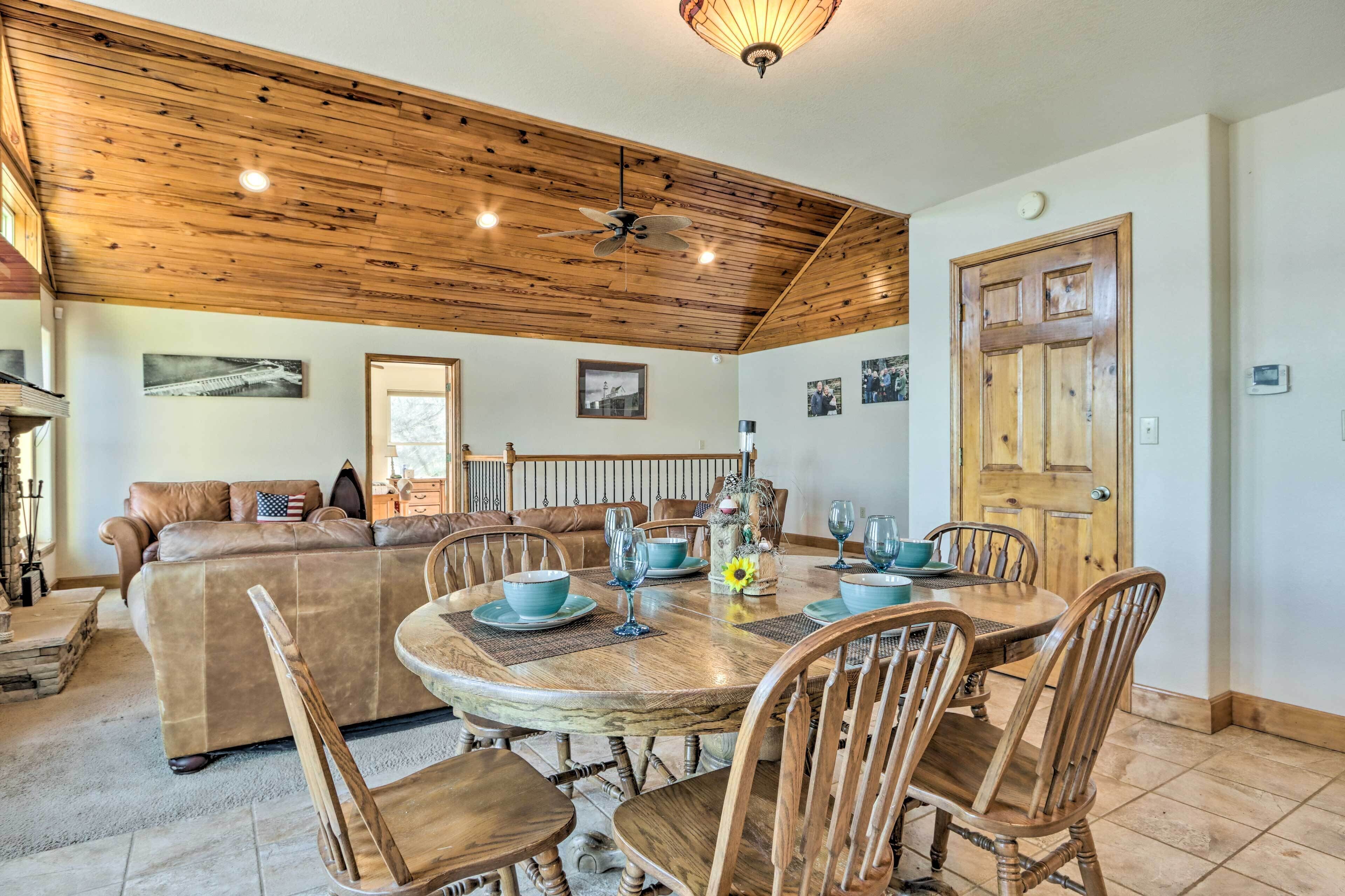 A dining area with a wooden ceiling, a round table with chairs, and a sofa in the background.