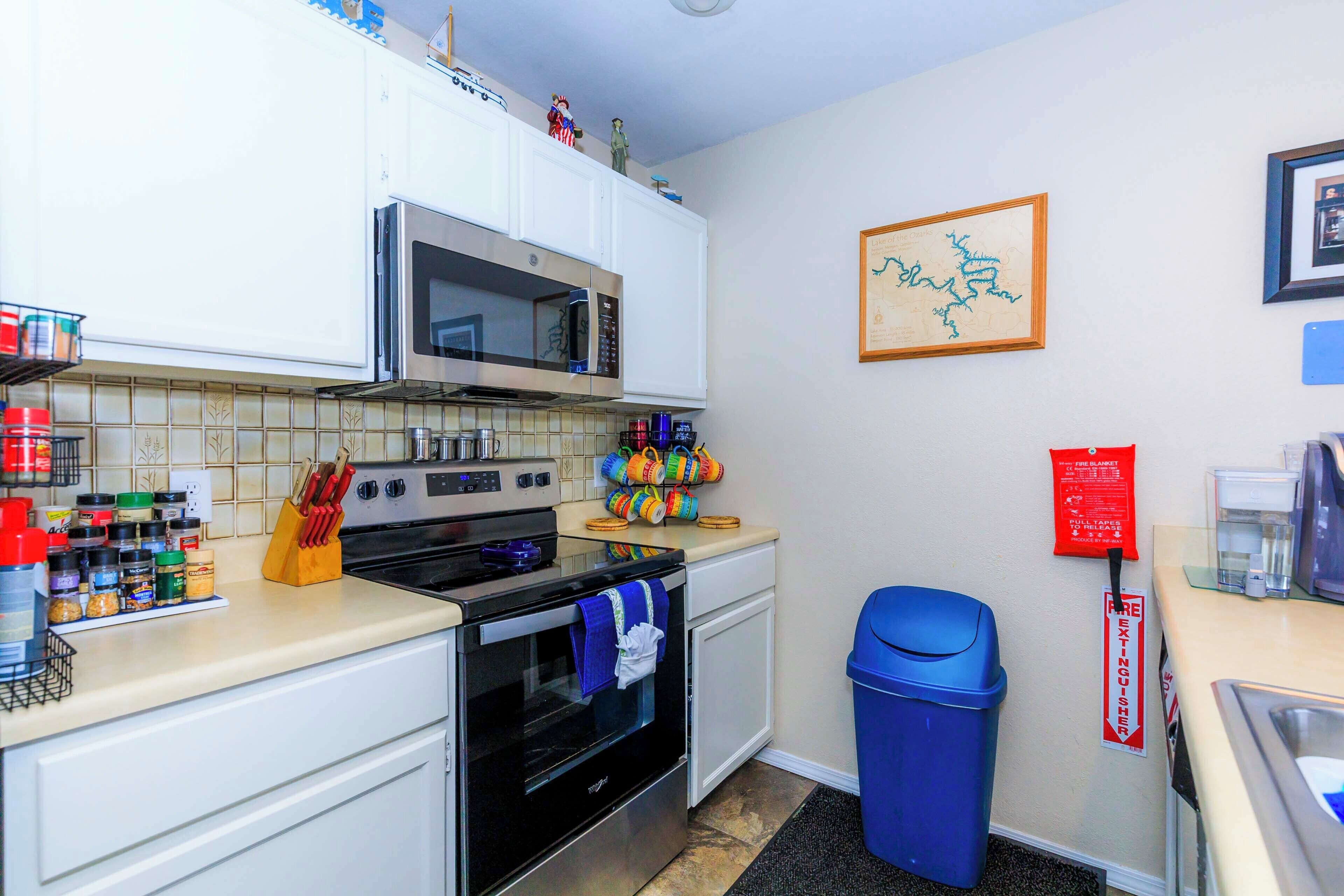 A kitchen with white cabinets, a microwave, an oven, and a blue trash bin.