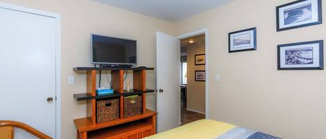 A bedroom with a bed, a television on a wooden stand, and framed pictures on the wall.