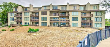 A multi-story residential building with balconies, a gravel courtyard, and a blue fence.