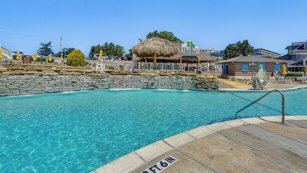 A swimming pool with a thatched roof structure, a stone wall, and a sign reading "The But." - Furnished Deck! Golfer's Oasis in Margaritaville (Osage Beach)