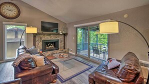 A cozy living room with a fireplace, leather sofas, a coffee table, and a large window overlooking a deck. - Furnished Deck! Golfer's Oasis in Margaritaville (Osage Beach)