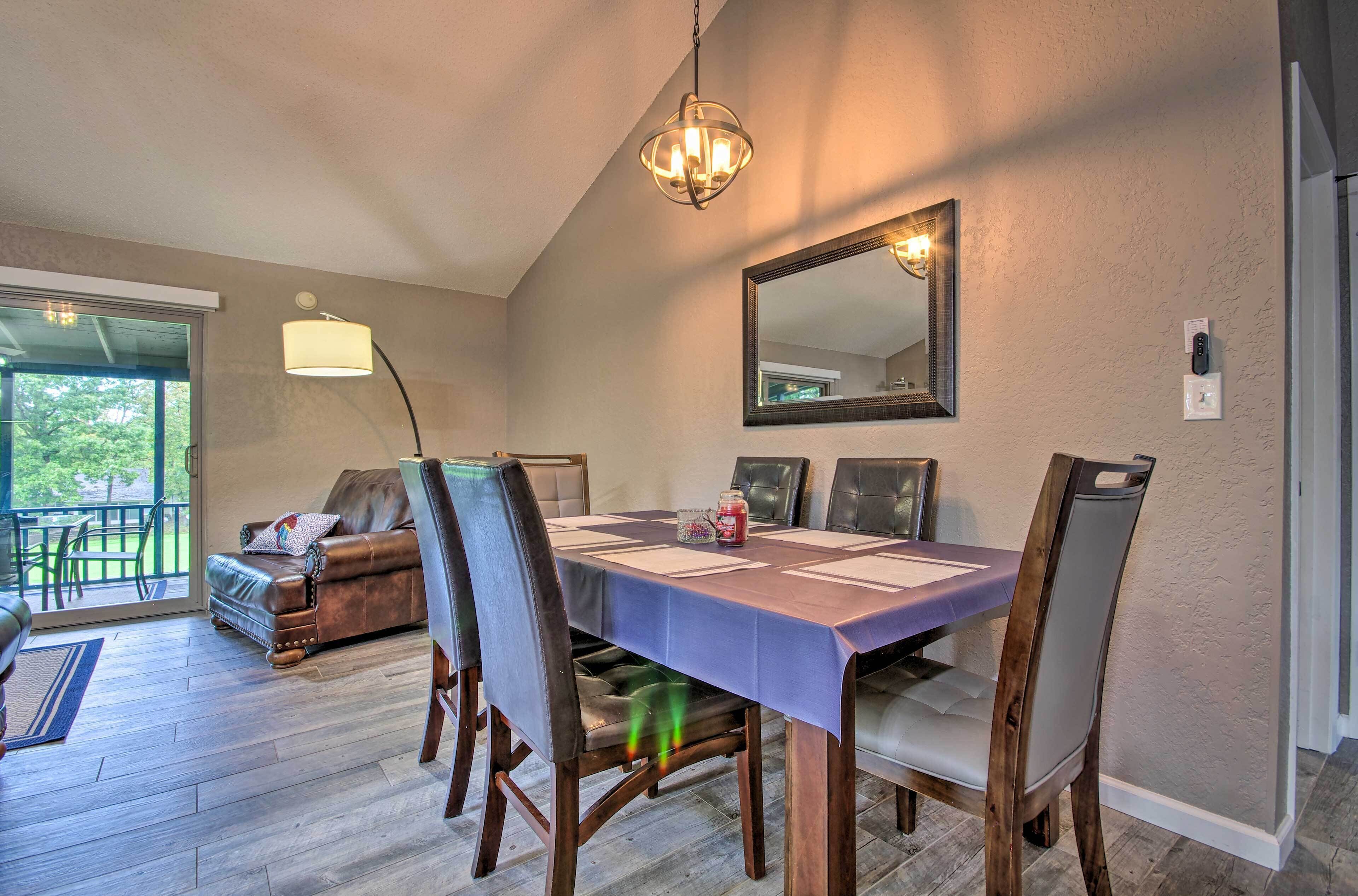 A dining area with a table set for four, surrounded by chairs, a chandelier, and a large mirror on the wall.