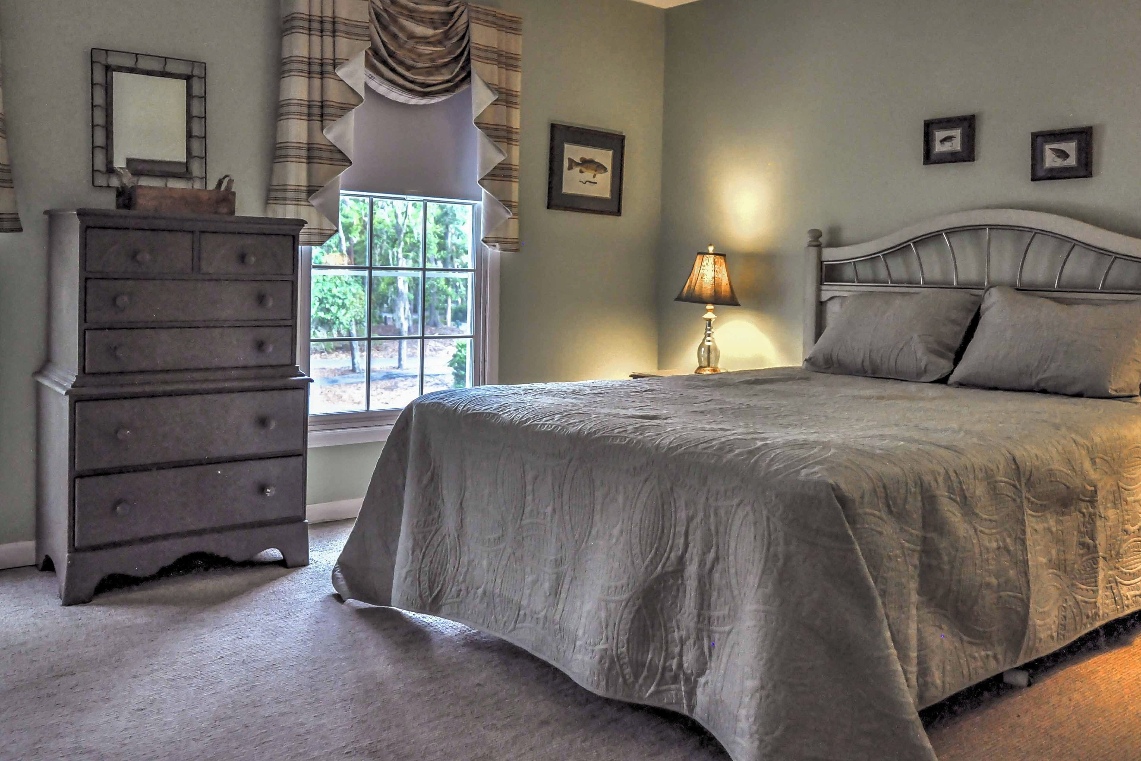 Une chambre à coucher avec un lit, une commode, une lampe et une fenêtre avec des rideaux.