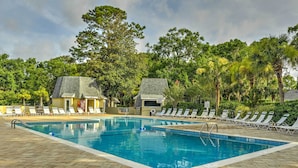 Une piscine rectangulaire, bordée d’une terrasse carrelée, entourée de chaises longues et de palmiers.