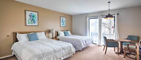 Une chambre d’hôtel avec deux lits, une table à manger, des chaises et des œuvres d’art accrochées aux murs.