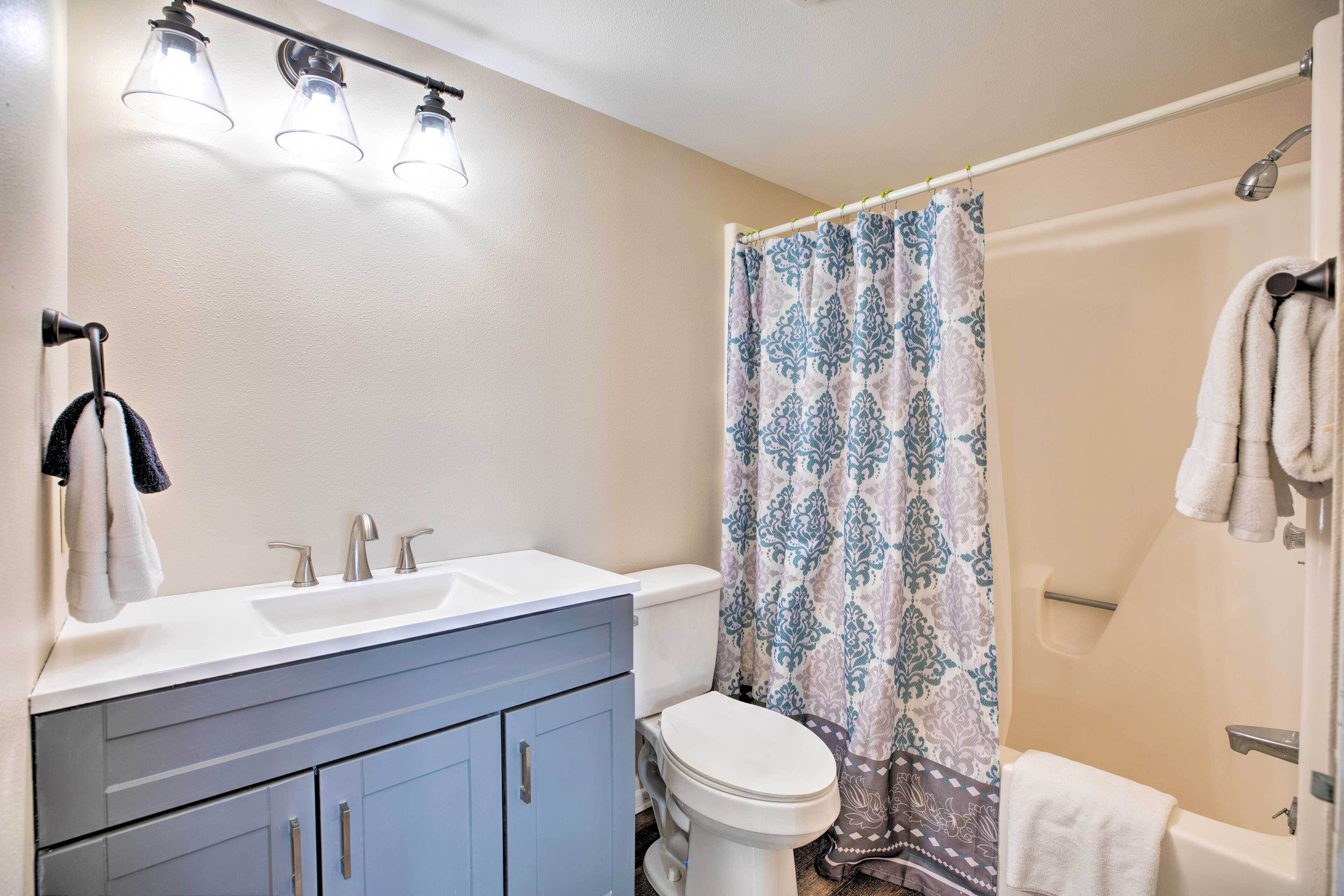 A bathroom with a double sink vanity, a toilet, a shower with a patterned curtain, and a bathtub with towels.