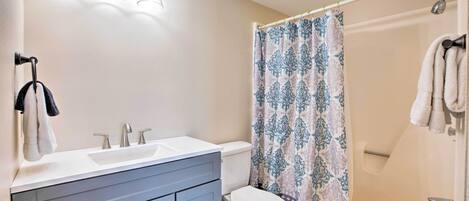 A bathroom with a double sink vanity, a toilet, a shower with a patterned curtain, and a bathtub with towels.