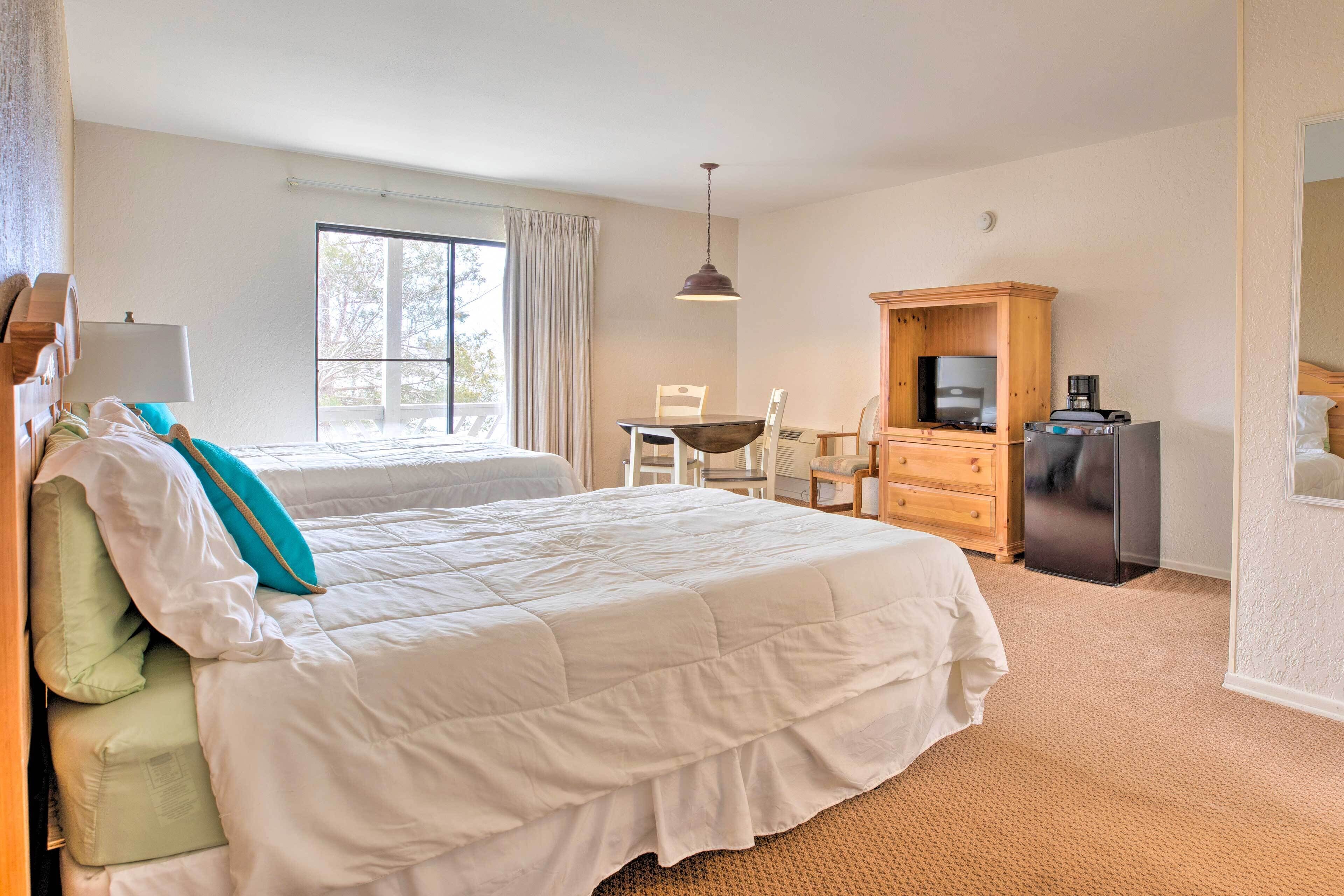 A hotel room with a large bed, a desk with a chair, a television, and a minibar.