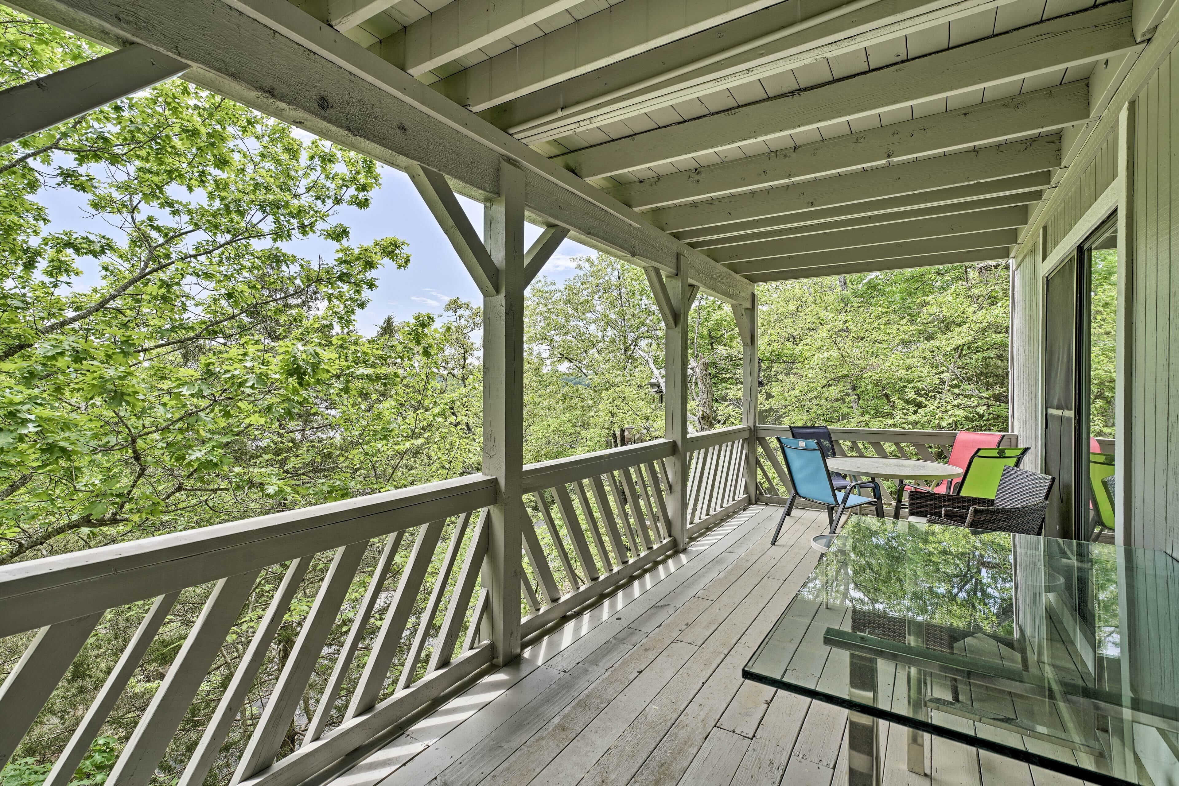 A covered porch with a glass table and chairs, surrounded by trees.