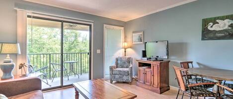 Een ruime woonkamer met een houten tafel, comfortabele zithoek, een televisie en een balkon met buitenmeubilair.