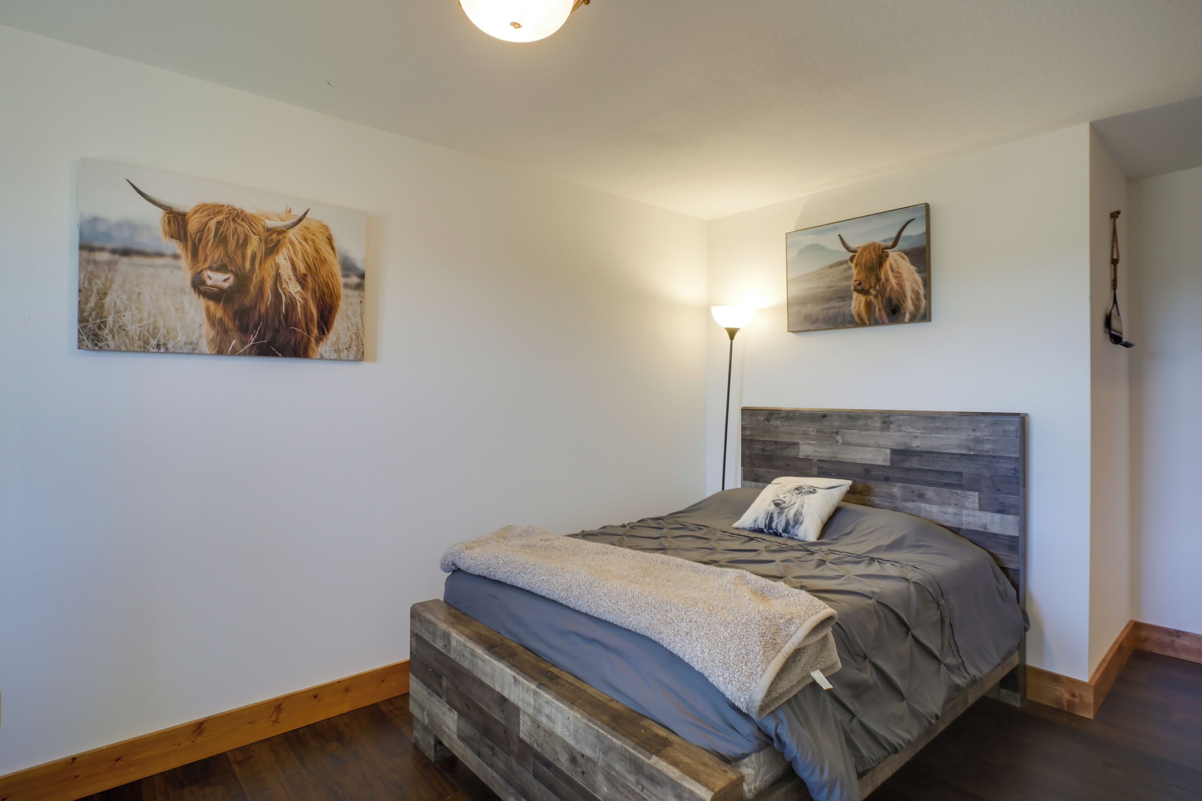 Un dormitorio con cabecera de madera, cama con ropa de cama gris y dos cuadros de vaca de las Tierras Altas en las paredes.