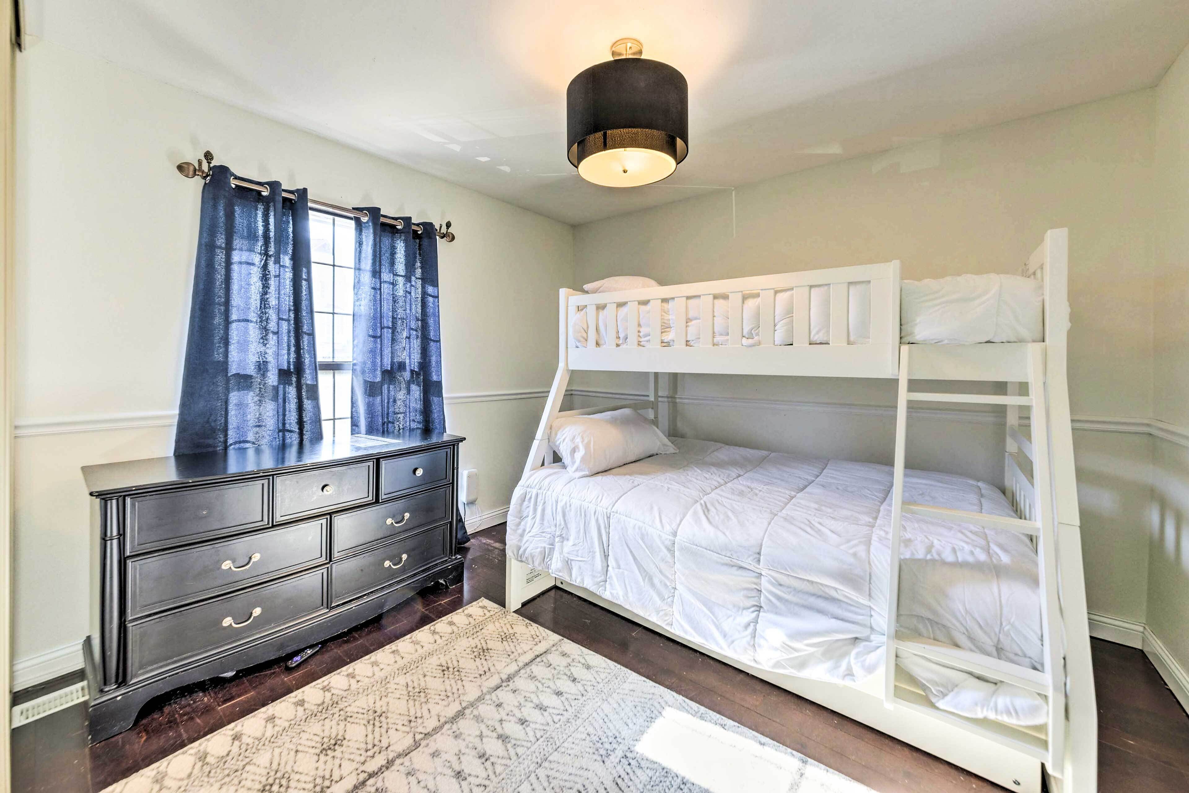 A bedroom with a bunk bed, a dresser, a window with curtains, and a ceiling light.