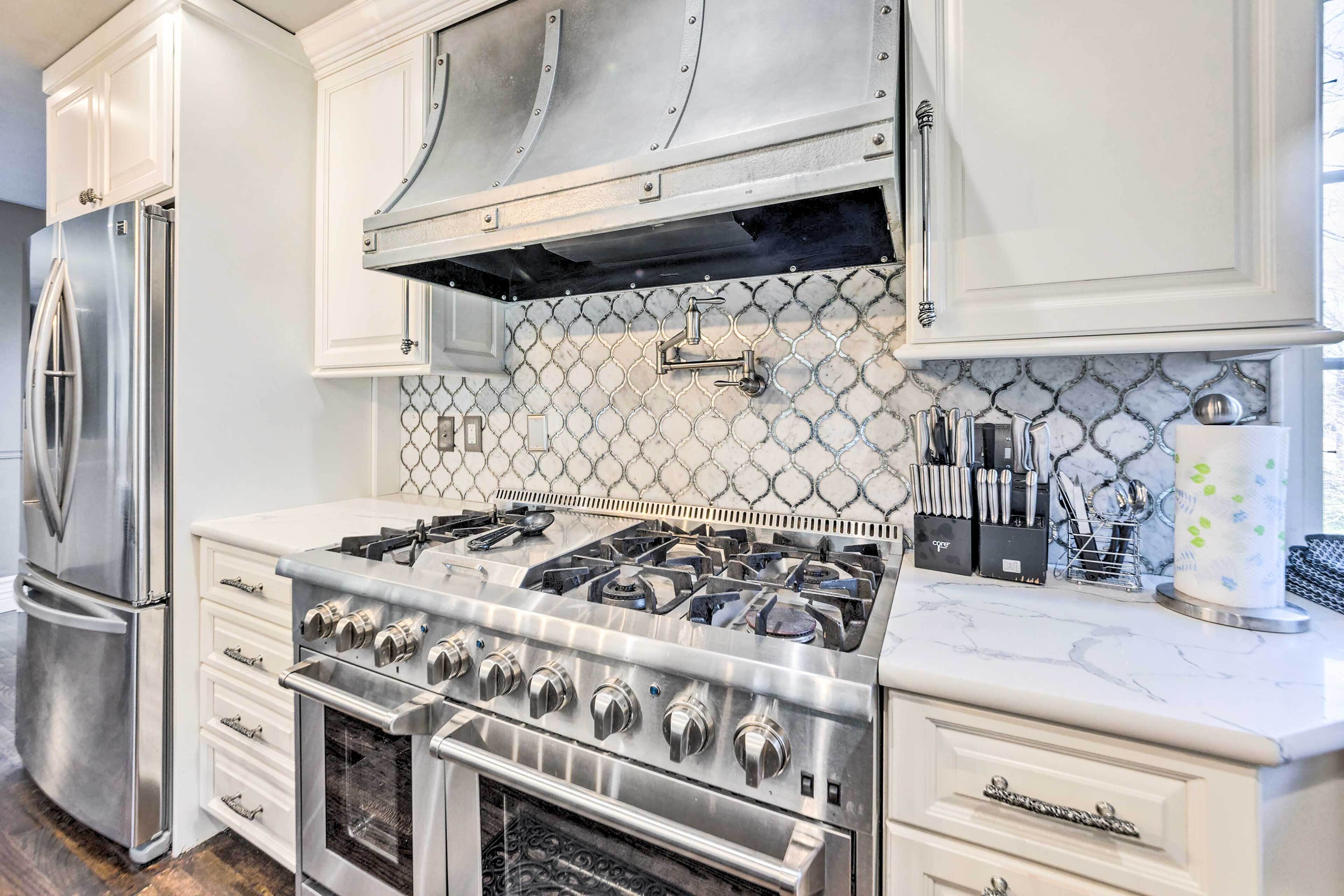 A kitchen with stainless steel appliances, white cabinetry, and a patterned backsplash.