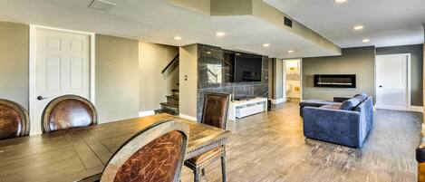 A spacious living area with a dining table, chairs, a sofa, and a flat-screen TV mounted on the wall.