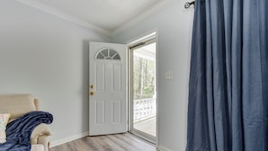 Una habitación con un sofá color beige, una manta azul oscuro, una puerta blanca y vistas a un balcón.