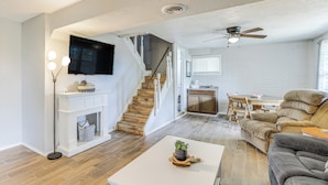 A spacious living area with a staircase, a flat-screen TV mounted above the fireplace, a ceiling fan, and a cozy seating arrangement. - Deck & Table Rock Lake View: Shell Knob Escape! (Shell Knob)