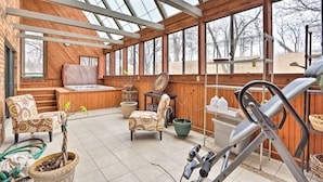 A spacious indoor area with a wooden floor, a hot tub, and a large window providing a view of trees. - Spacious Home w/ Pond ~ 13 Mi to Columbia! (Hallsville)