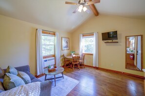 A living room with a ceiling fan, a television mounted on the wall, and a dining area with a table and chairs.