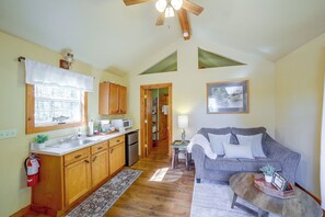 A cozy interior with a kitchen, dining area, and living room, featuring wooden cabinets, a microwave, and a grey sofa.