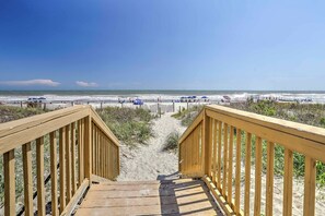 A wooden staircase leading to a sandy beach with umbrellas and people in the distance.