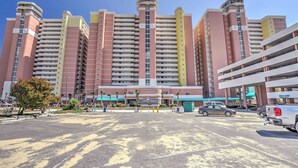 Ein mehrstöckiges Hotel mit zentralem Eingangsbereich, Parkplatz und blauem Himmel.