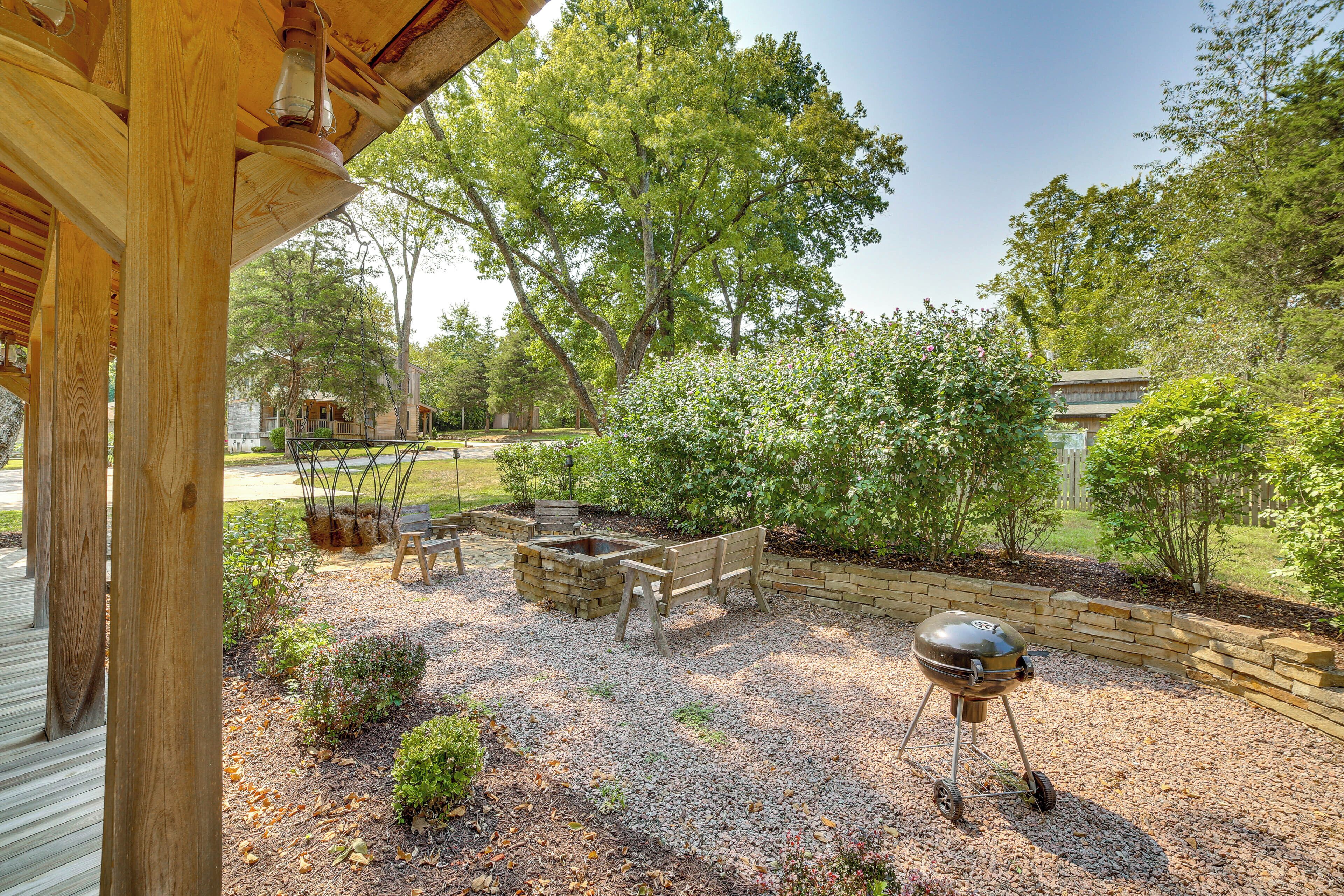 A covered outdoor area with a barbecue grill, wooden benches, and a fire pit.